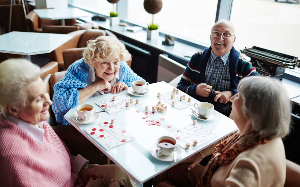 Group of elderly people sitting by table, talking and playing lotto
