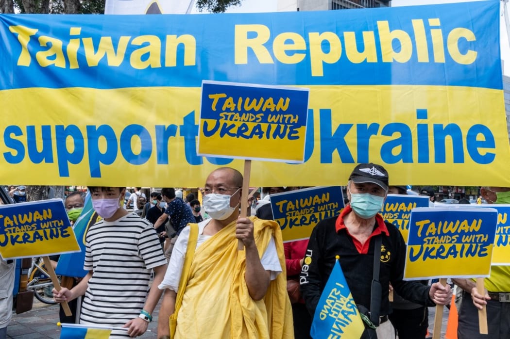 Group of People standing in front of a big banner reading the Taiwan Republic supports Ukraine while holding signs and banners in the colours of Ukraine reading Taiwan stands with Ukraine. Taipei, Taiwan. Sunday, March 13 of 2022.