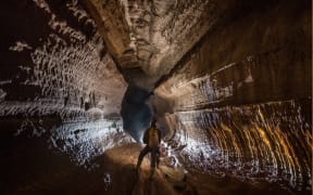 An image from inside the Armageddon cave system, showing a caver standing in  in a high and wide chamber.