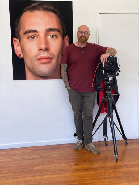 Photographer Charlie Fox with his camera on a stand and a portrait he took of Daniel Heaphy in 2016 hanging on the wall behind him.