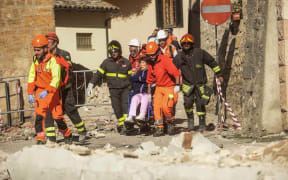 Firefighters and rescuers in Norcia carry a woman on a wheelchair after the quake.