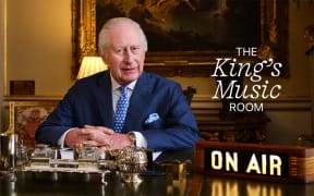 King Charles sits in his office in Buckingham Palace, an 'ON AIR' sign to his right and a graphic reading 'The King's Music Room' next to him.