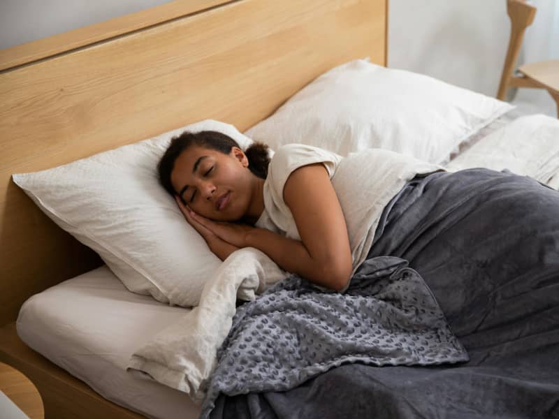 A brown-skinned woman sleeps under blankets.
