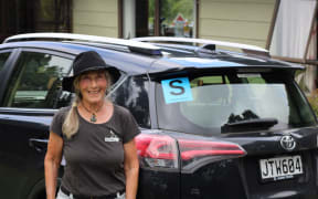 A woman standing near a car with the S sticker on the rear windshield.