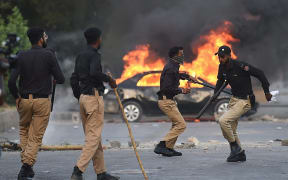 Policemen retreat after firing teargas shells towards Pakistan Tehreek-e-Insaf (PTI) party activists and supporters of former Pakistan's Prime Minister Imran near burning car during a protest against the arrest of their leader in Karachi on May 9, 2023. Former Pakistan prime minister Imran Khan was arrested on May 9, police said, during a court appearance for one of dozens of cases pending since he was booted from office last year. (Photo by Asif HASSAN / AFP)