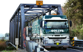 Road freight truck squeezing through one lane bridge.