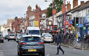 A man wearing a mask crosses Soho Road in Birmingham, England.