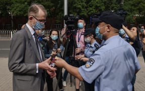 A Chinese police officer returns an ID card to Australian Ambassador to China Graham Fletcher (left) as he arrives at the Beijing Second Intermediate People's Court before the trial of Australian academic Yang Hengjun on May 27, 2021.