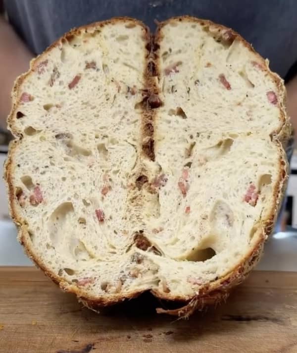 A loaf of bread cut in half shows small chunks of meat inside.