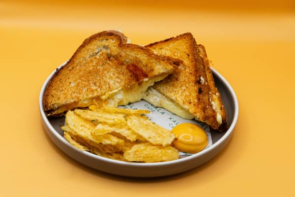 A plate of grilled cheese toastie and chips with mustard dip.