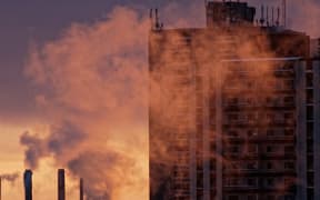 Smoke from a chimney rises over a city skyline in Canada.