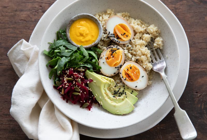 A bowl containing avocado, soy marinated eggs, greens and a carrot miso dressing.