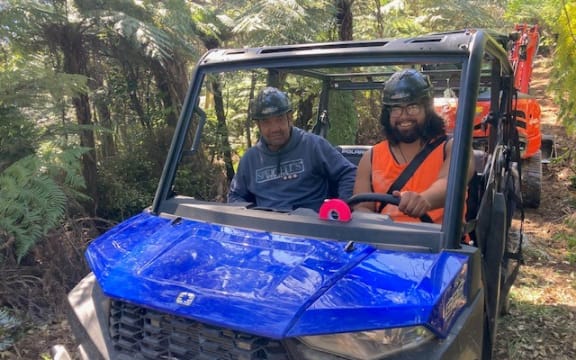 Two men in a golf cart-like vehicle in the bush. They are preparing to do track clearing work.