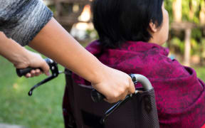 A care worker pushes an elderly woman in a rest home out for fresh air.