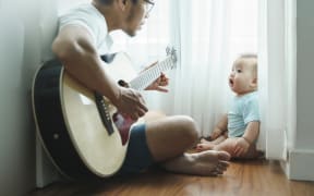 Father playing acoustic guitar to baby