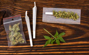 50549923 - marijuana background. cannabis joint, bud in plastic bag and hemp leaves on wooden table. addictive drug or alternative medicine.