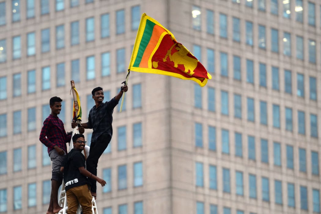 A man waves Sri Lanka's national flag after climbing a tower near presidential secretariat in Colombo on 1 July, 2022, after it was overrun by anti-government protesters.