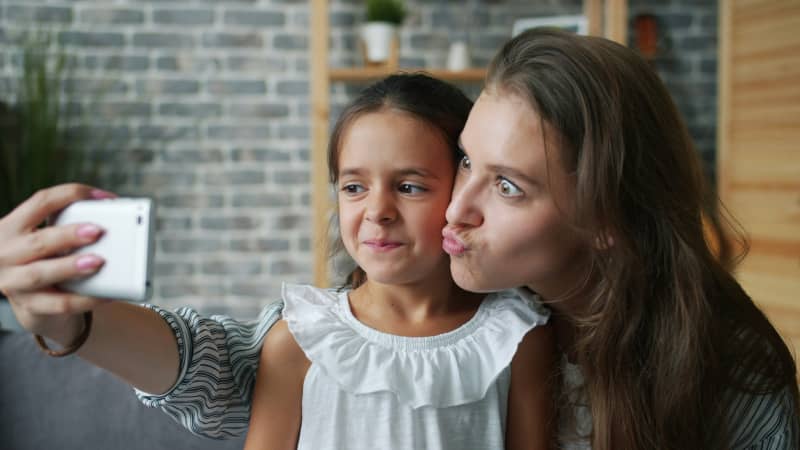 A young girl and her mother make faces for a selfie taken by the mother.