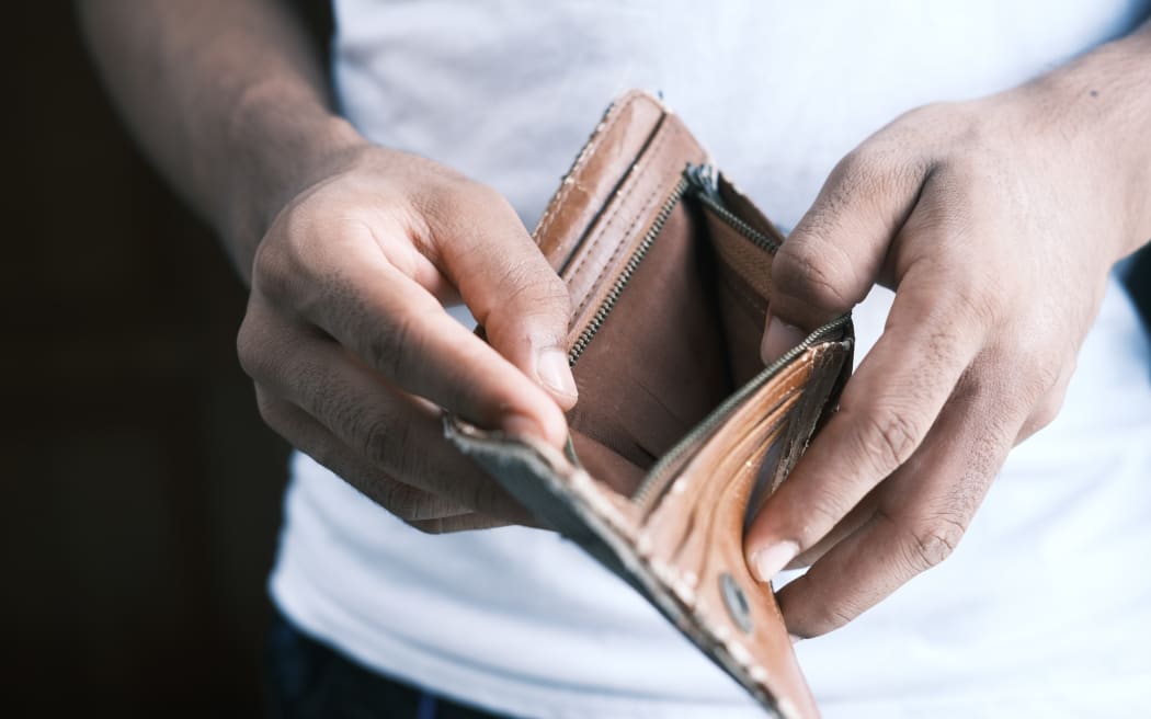 A person in a white t-shirt showing an empty wallet.