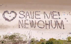 A group of people form the words "Save New Chum" on the beach. The photo is taken from the air.
