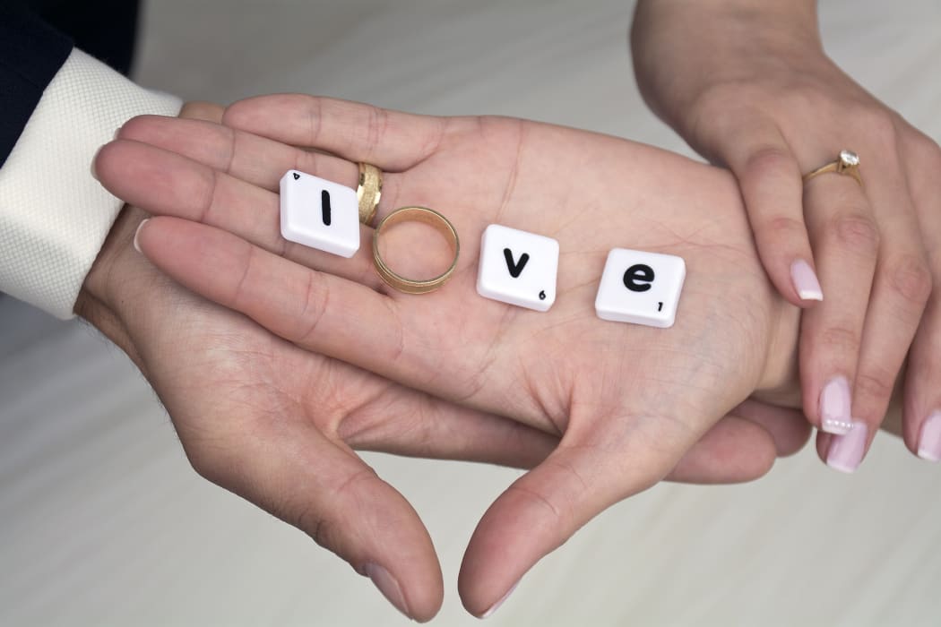 A hand with scrabble letters and an engagement ring spelling love.