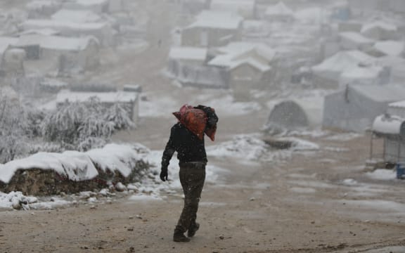 A man carries a sac of charcoal for heating following a snow storm at a camp for some 700 internally displaced Syrians from southern Idlib in Syria's Afrin region in the rebel-held northern Aleppo province on 5 February, 2023.