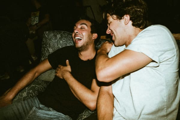 Two men laugh together on a couch.