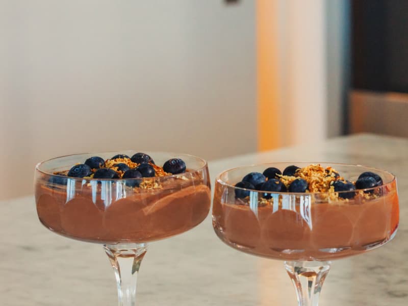 Two glass sundae dishes containing chocolate mousse, decorated with coconut and blueberries.