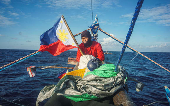 A man on a small boat in the middle of the sea holding the Philippines flag.