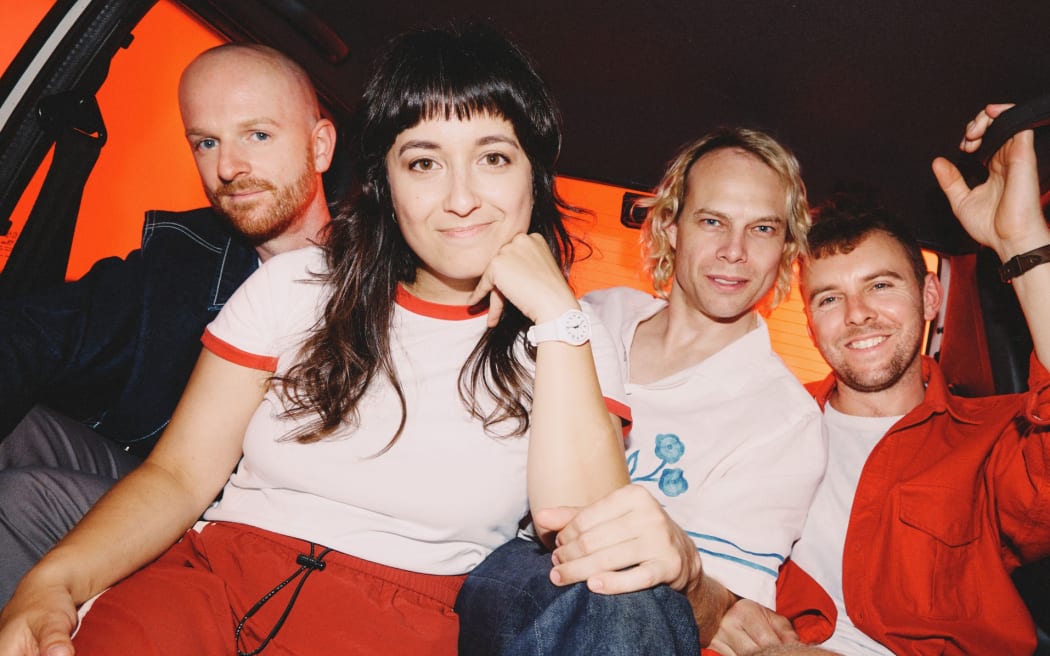 Four band members all bunched up sitting in the back of a car