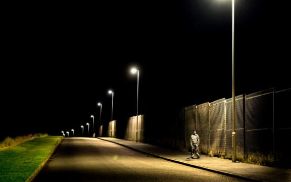 Boy standing on pavement at night with street lights (Photo by Craig Easton / Image Source / Image Source via AFP)