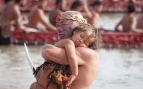 Wiremu Keretene (Ngāti Hine) holds a sleeping child during the waka display at Tii Beach this morning.