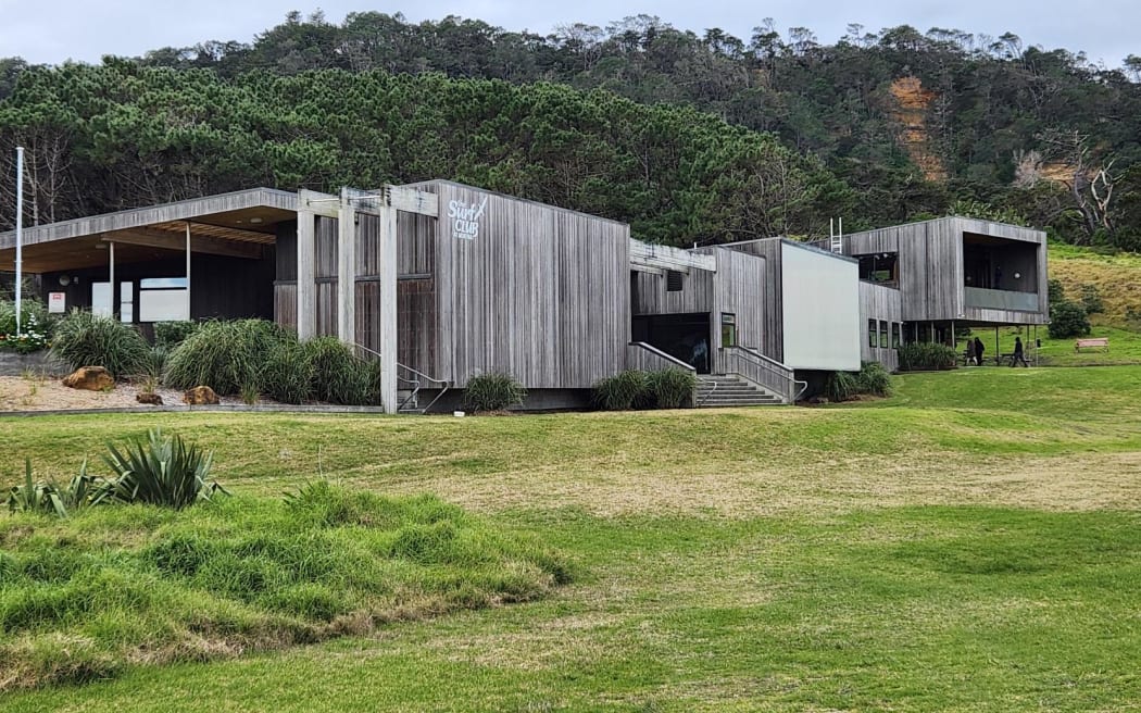 A large, modern looking building surrounded by grass and forest in the background.