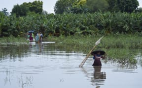 Stranded people wade through a flooded area after heavy monsoon rainfall in the Nawābshāh district of Sindh province, southern Pakistan on 25 August, 2022.