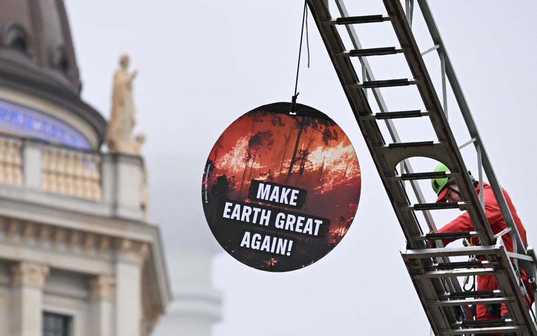 A Greenpeace environmental activist installs a round placard reading "Make the world great again" with landmark TV tower in the background in front of Germany's Foreign Ministry where the Petersberg Climate Dialogue (PCD) conference is held, on March 26, 2025. (Photo by RALF HIRSCHBERGER / AFP)