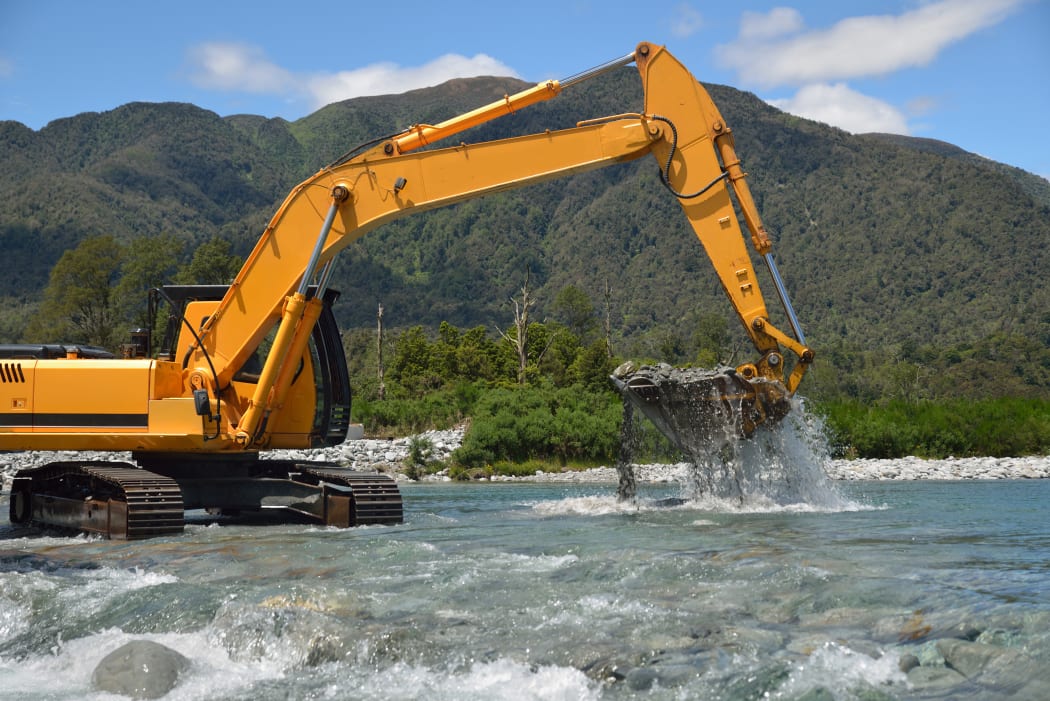 digger shifting shingle to deepen the channel in a flowing river, Westland, New Zealand