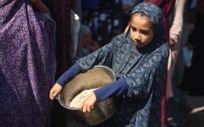 A Palestinian girl carries a bowl of rice after receiving a food portion from a charity kitchen in Deir el-Balah, Gaza Strip, on October 8, 2025. (Photo by Majdi Fathi/NurPhoto) (Photo by MAJDI FATHI / NurPhoto via AFP)