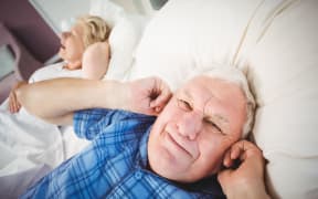 Senior man covers ears while wife snores
