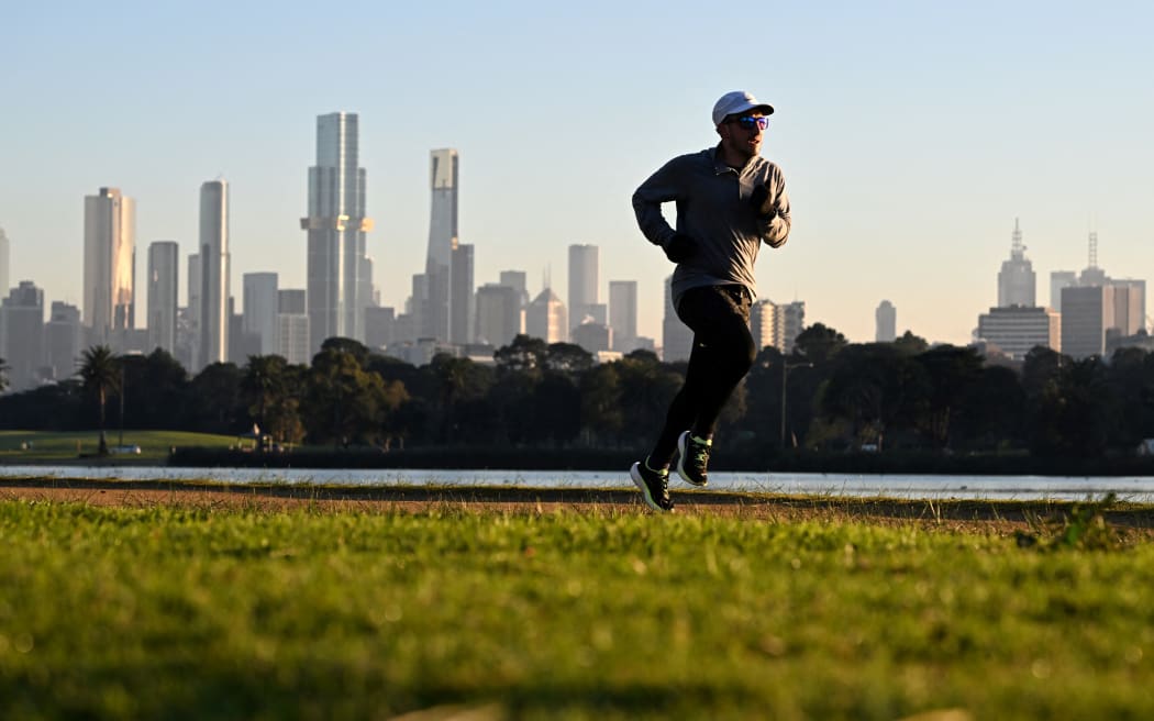 With the Melbourne skyline in the background, a jogger takes part in an early morning fun run around Albert Park Lake as Melbourne awoke to freezing conditions on July 3, 2024. (Photo by William WEST / AFP)