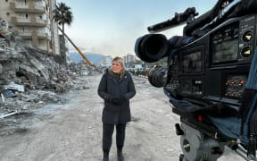 Correspondent Lisette Reymer standing in the rubble for a morning live cross after a night of camping out in a car amid constant earthquake aftershocks in Turkey.