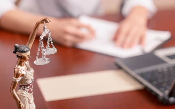 Follow the law. Professional lawyer sitting at the table and signing papers with justice statue standing on surface in forefront.