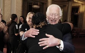 Britain's King Charles III reacts as he is hugged by members of New Zealand's Black Ferns rugby team at Buckingham Palace, 2024.