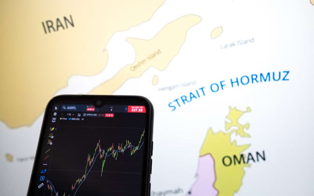 A stock exchange curve appears on a smartphone screen, and a map shows the Strait of Hormuz on a laptop computer screen in this photo illustration taken in Athens, Greece, on March 3, 2026. (Photo by Nikolas Kokovlis/NurPhoto) (Photo by Nikolas Kokovlis / NurPhoto via AFP)
