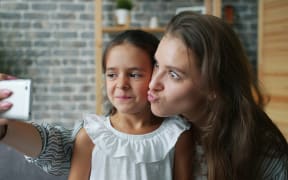 A young girl and her mother make faces for a selfie taken by the mother.