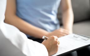 A medical professional takes notes while talking to a female patient.