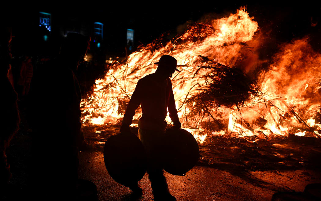A Tar Barrel Man walks past a fire at the end of the procession through the streets of Allendale during the annual Allendale Tar Barrel festival in Allendale, northern England, on the night between December 31, 2024 and January 1, 2025. - The Tar Barrel Festival is a New Year celebration in the Northumberland village of Allendale which dates back to 1858. The festival involves a procession of 45 men carrying burning barrels filled with tar, sawdust, kindling and paraffin on their heads. Shortly before midnight the men return to the village square to light a bonfire by throw on their burning barrels. (Photo by Oli SCARFF / AFP)