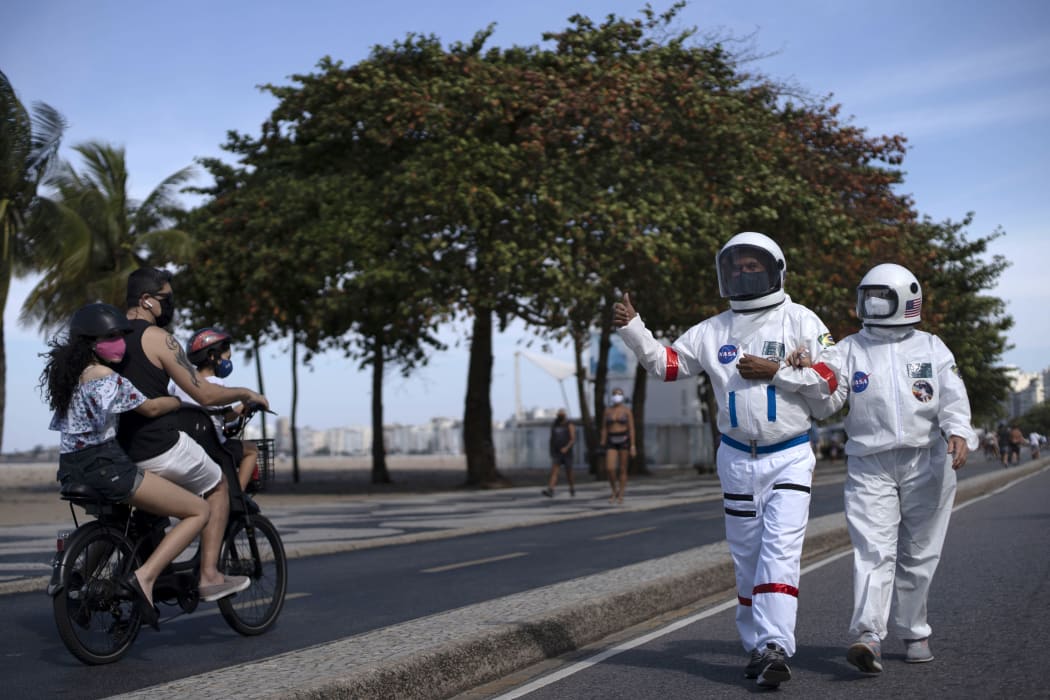 Brazilian accountant Tercio Galdino, 66, gives the thumb up to people riding a motorcycle as he and his wife Alicea Galdino walk along Leme beach in protective suits, in Rio de Janeiro, Brazil on July 12, 2020.