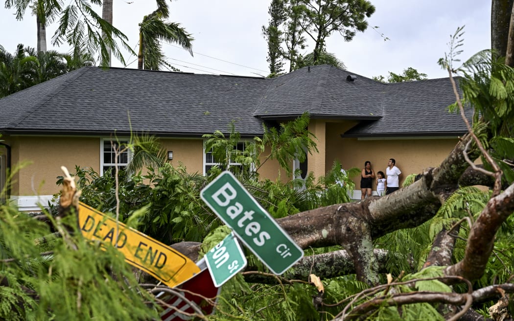 Oscar Garcia, right, with his family stands outside his house after getting hit by a reported tornado in Fort Myers, Florida, on 9 October 2024, as Hurricane Milton approaches.  (Photo by CHANDAN KHANNA / AFP)