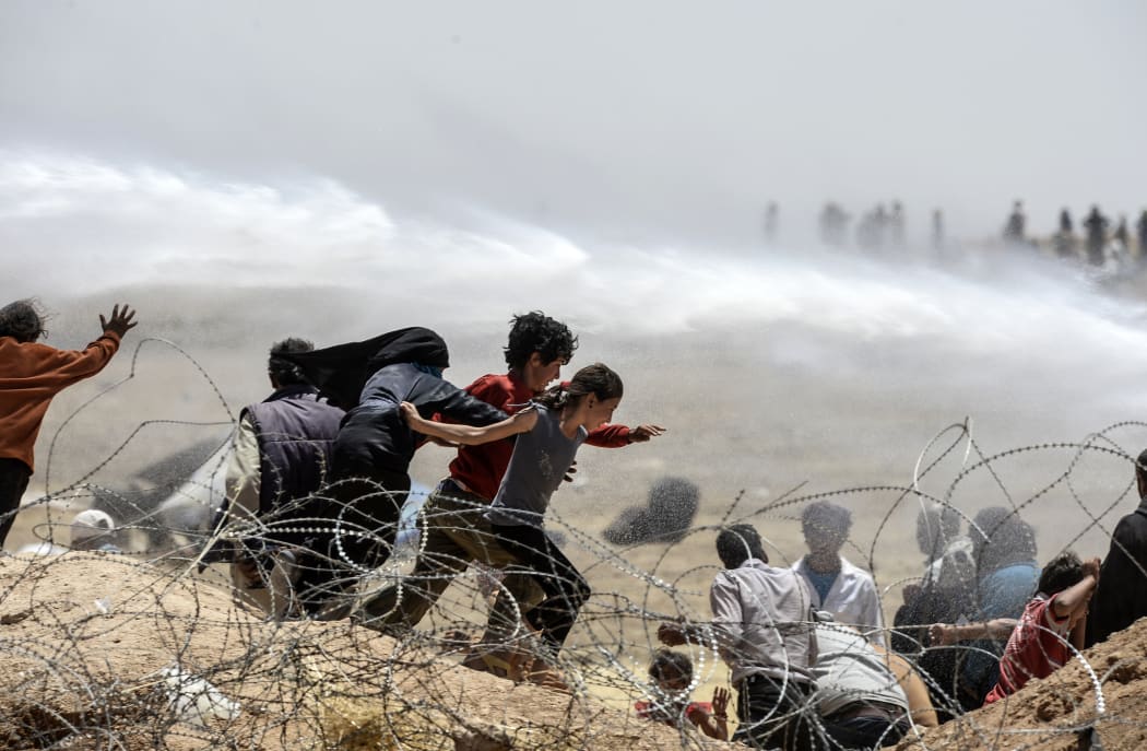 Syrian refugees run away as Turkish soldiers use water cannon to move them away from fences at the Turkish border near the Syrian town of Tal Abyad, at Akcakale in Sanliurfa province, on June 13, 2015.