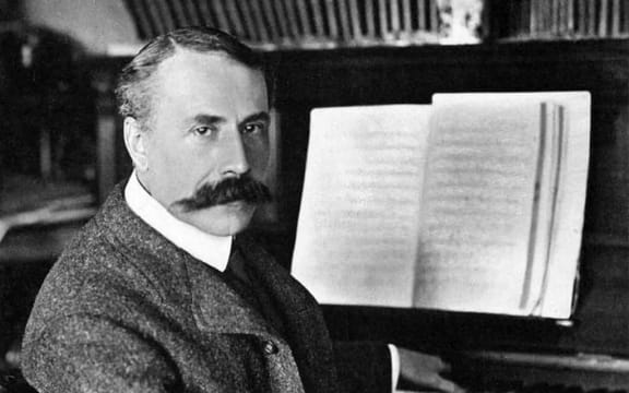 Composer Edward Elgar, seated at a piano, looking towards us, around 1900.